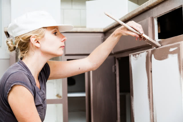Kobieta malująca pędzlem szafki w kuchni